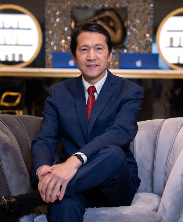 Dr. Pu in suit seated on grey chair.