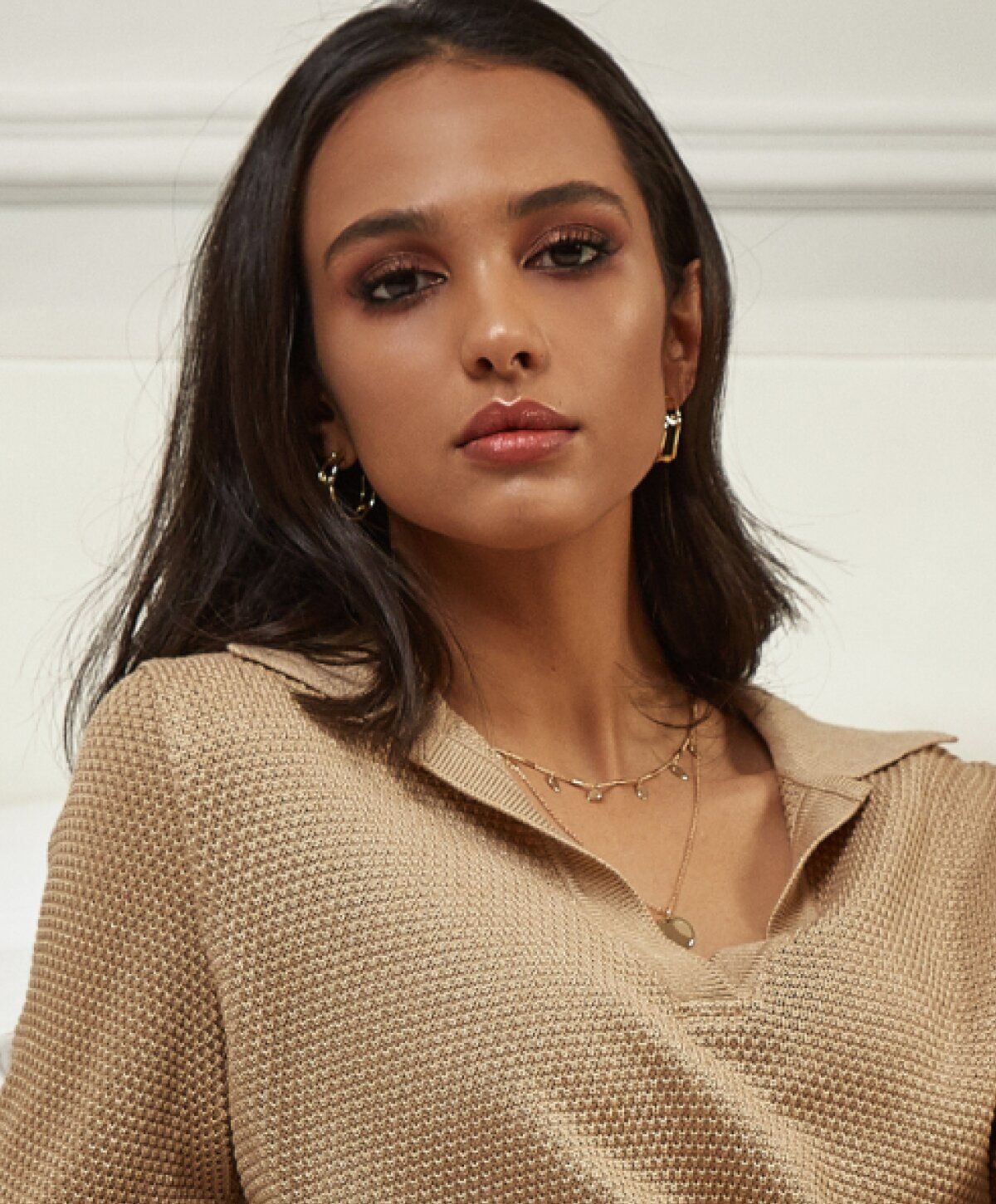 Model wearing a beige sweater and jewelry.