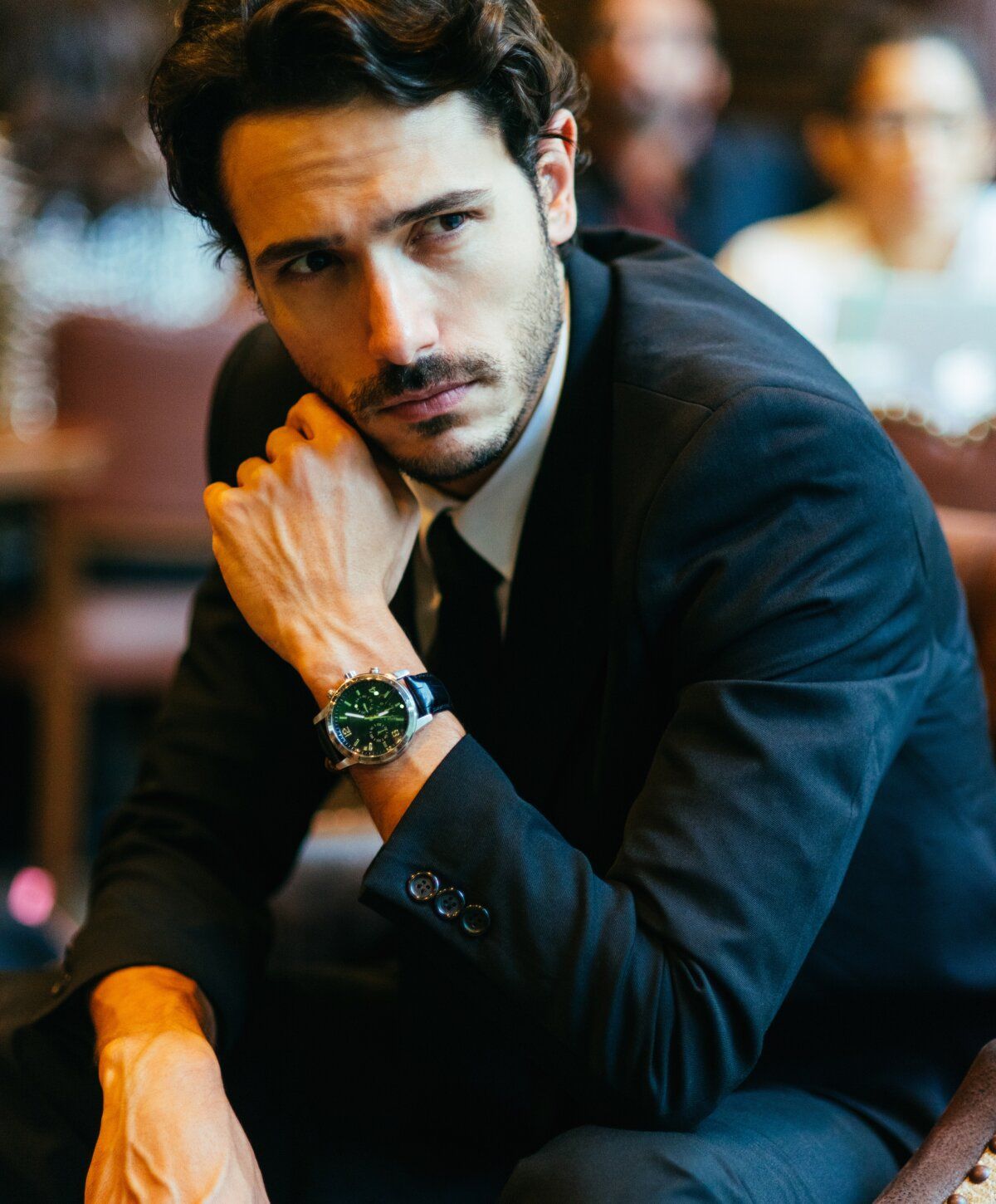 Man in suit with watch, deep in thought.