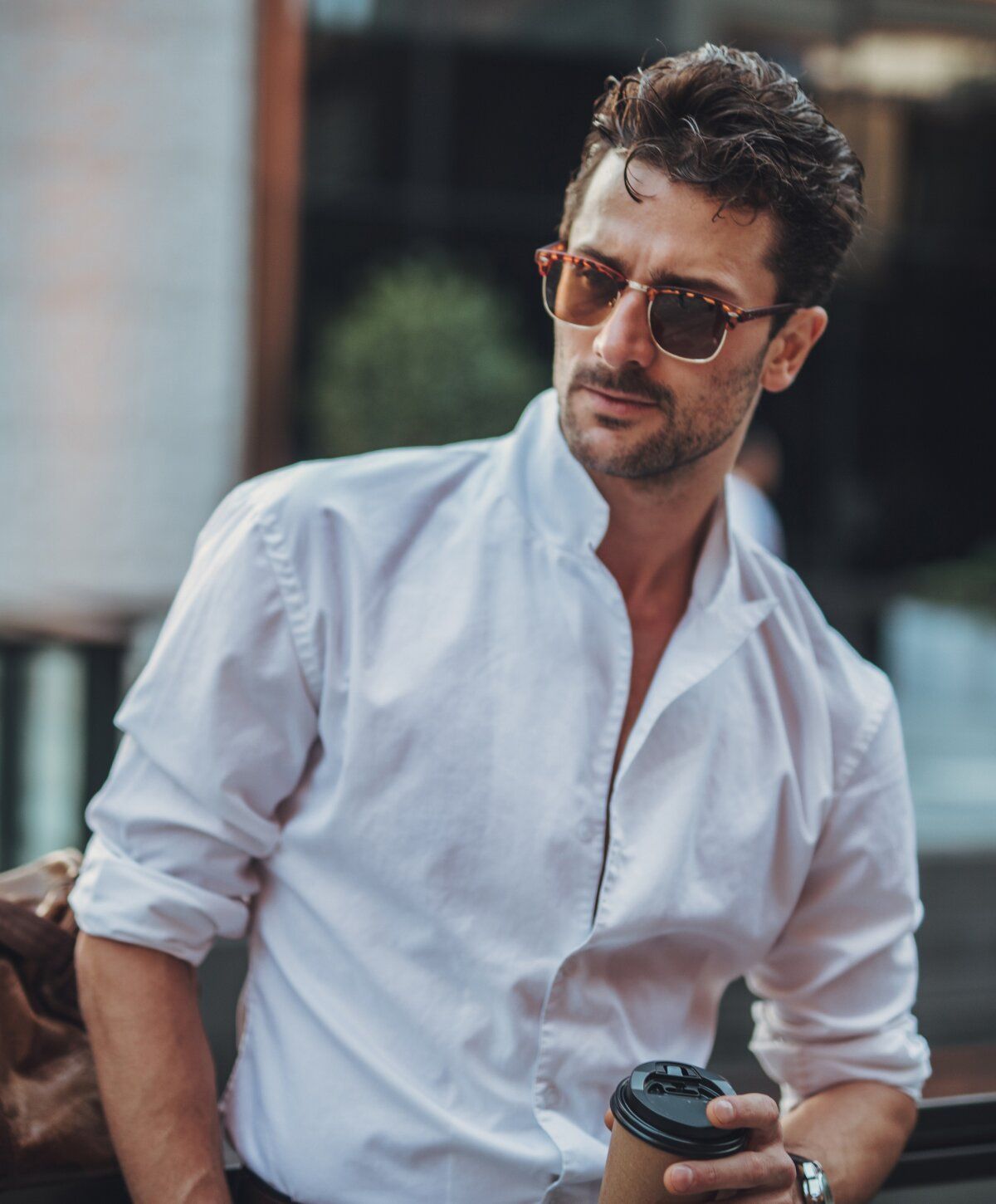 Man in sunglasses holding coffee cup outdoors.