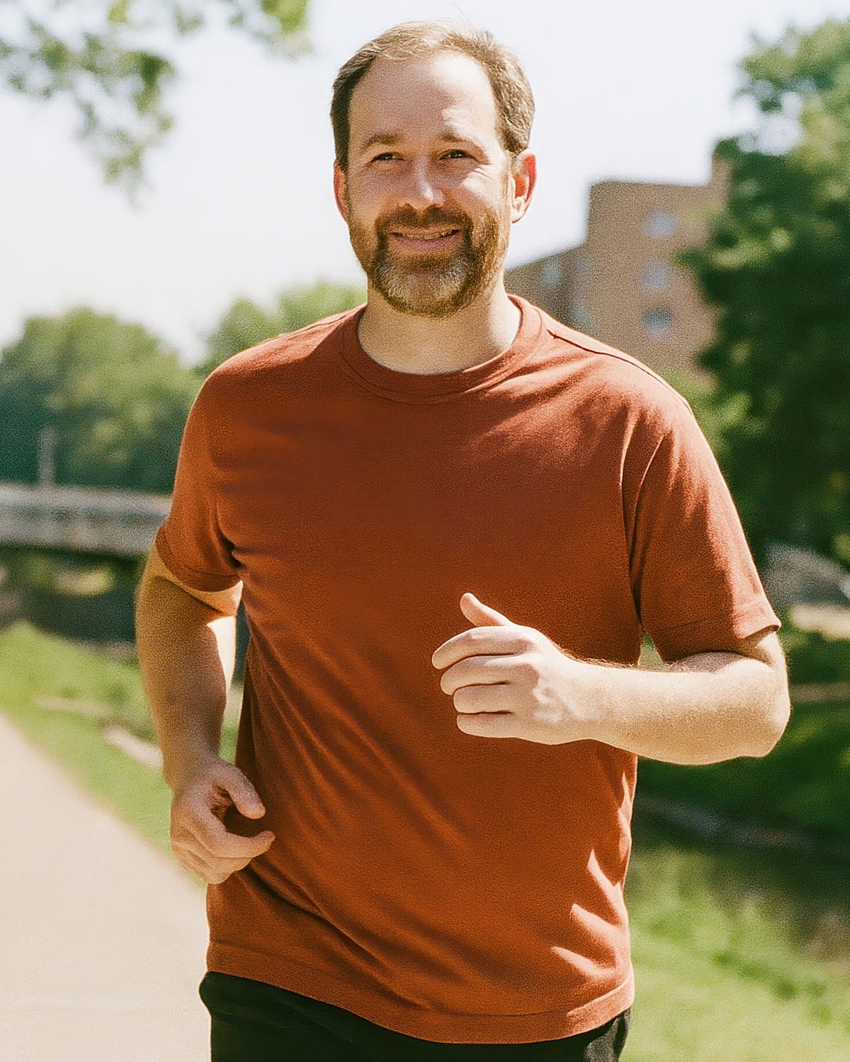 Smiling man jogging outdoors in casual attire.