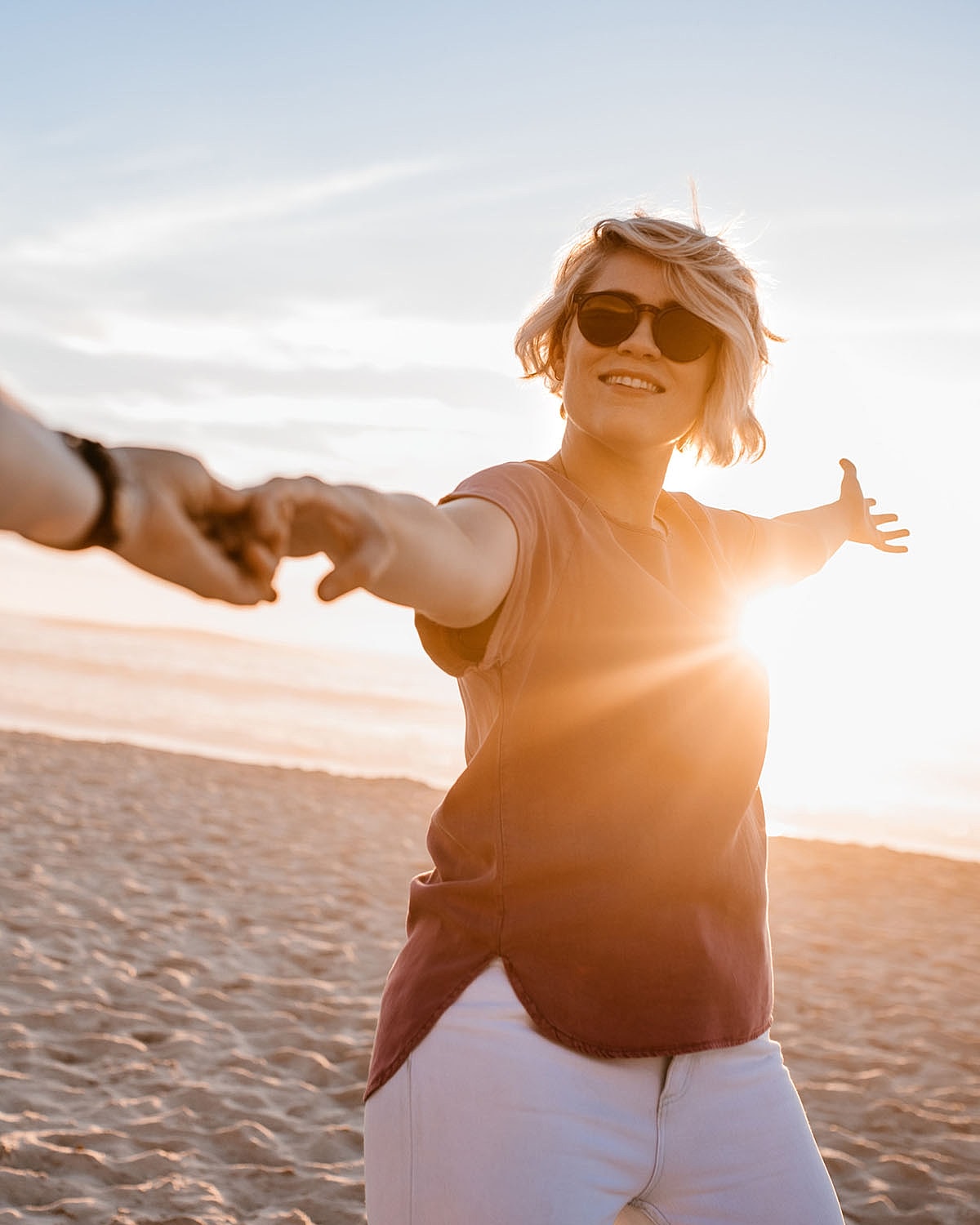 Woman enjoying sunset on beach, arms outstretched.