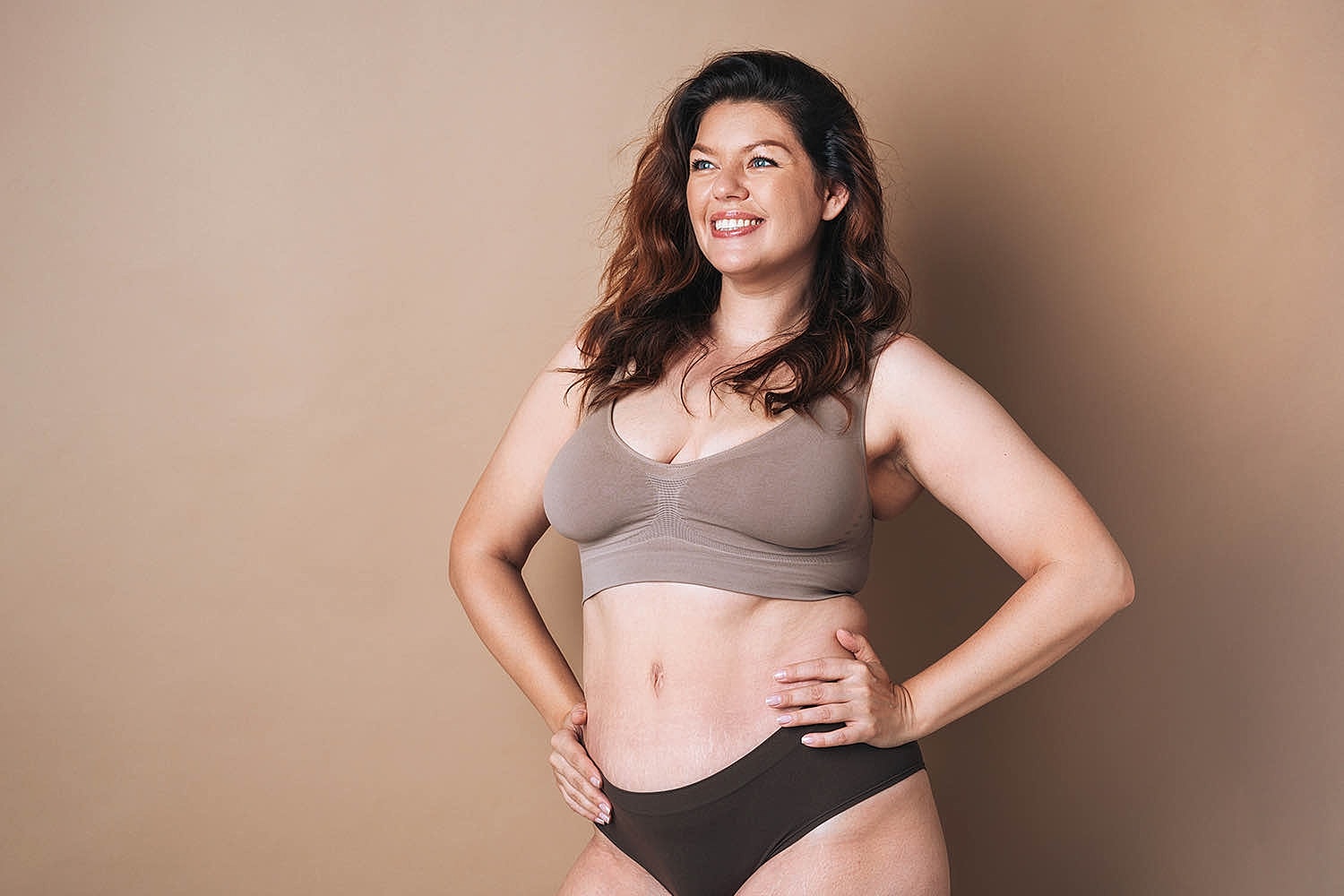 Model in beige activewear lounging on a surface.