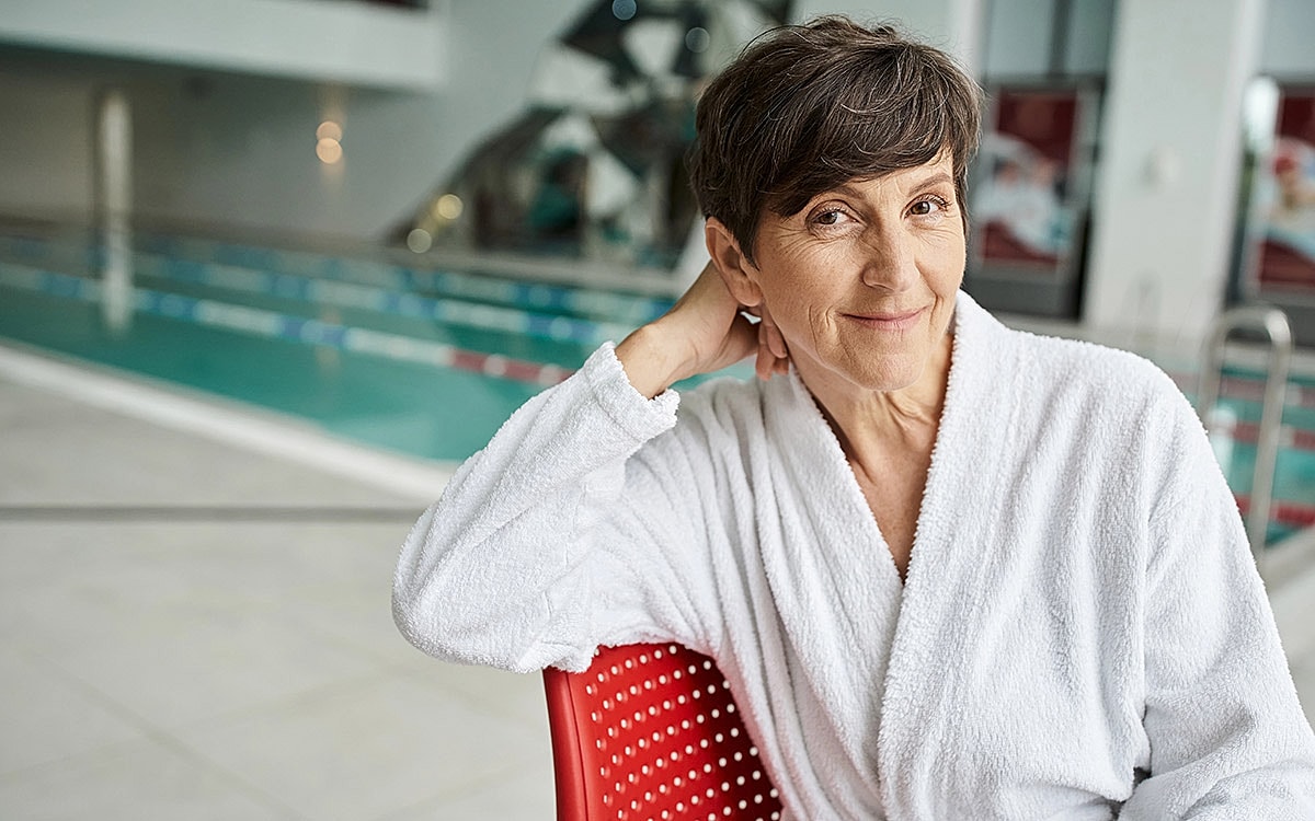 Smiling woman in white robe by swimming pool.
