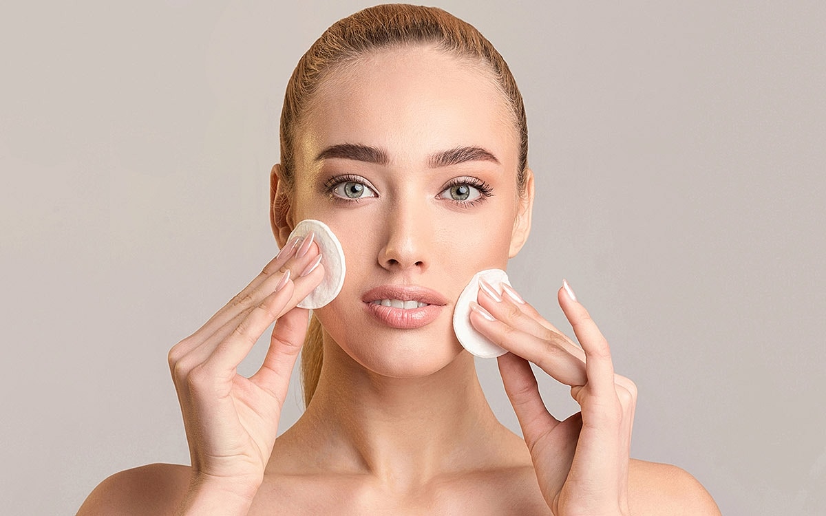 Woman applying skincare with cotton pads.