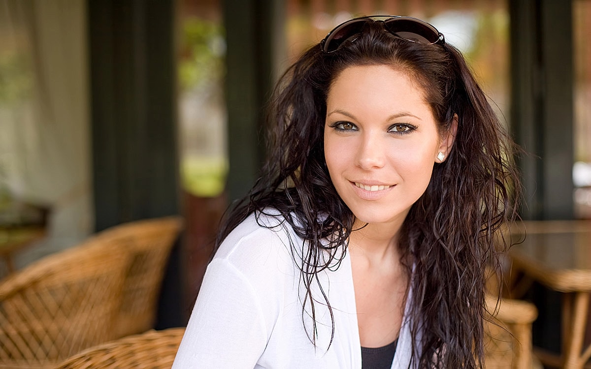 Woman smiling with wavy hair in cafe setting.