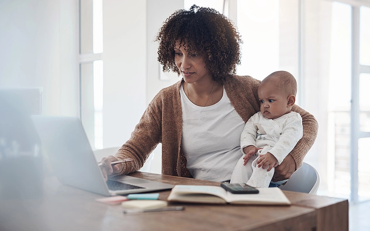 Mother working on laptop with baby in arms.