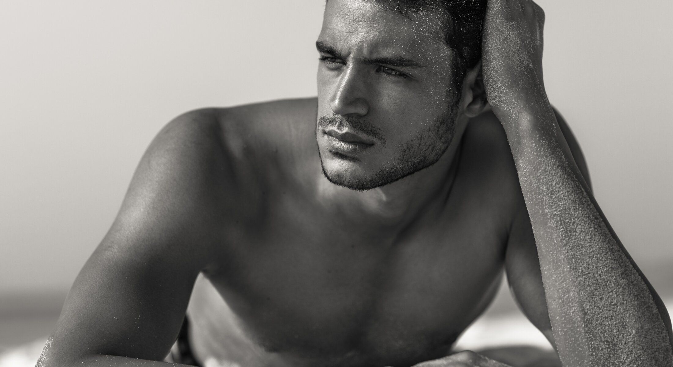Man lying on beach, thoughtful expression, black and white.