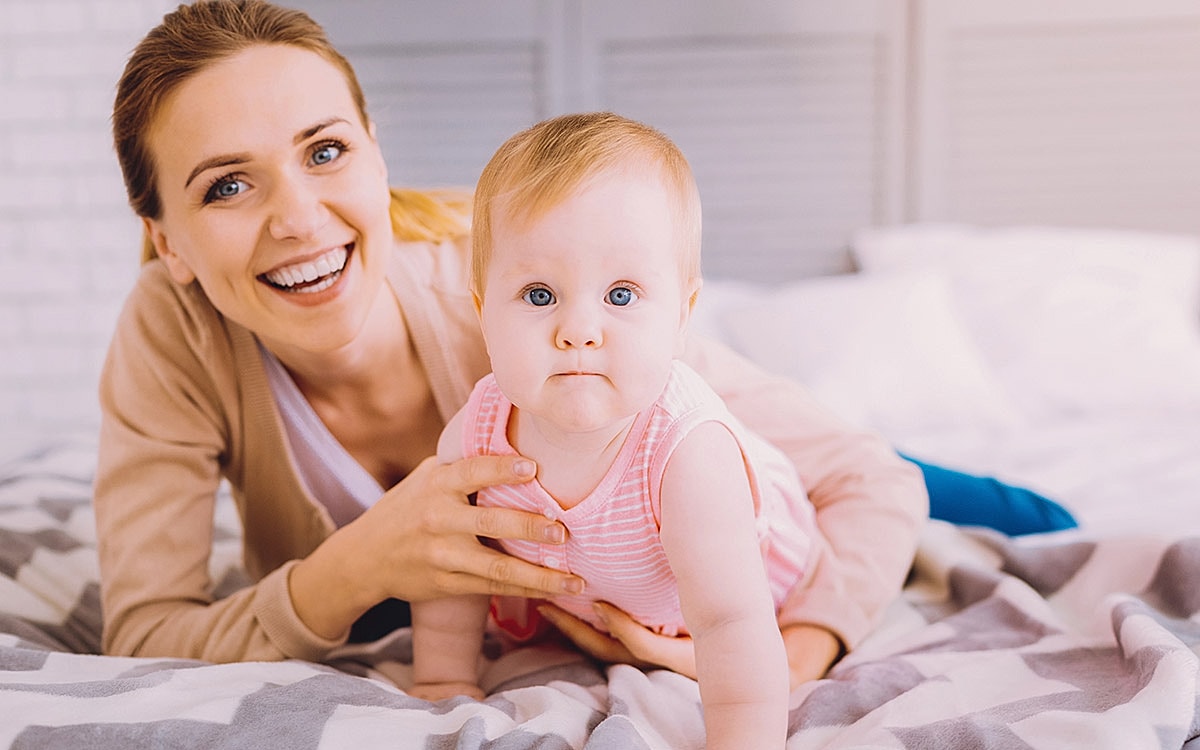 Smiling mother and baby on bed together.