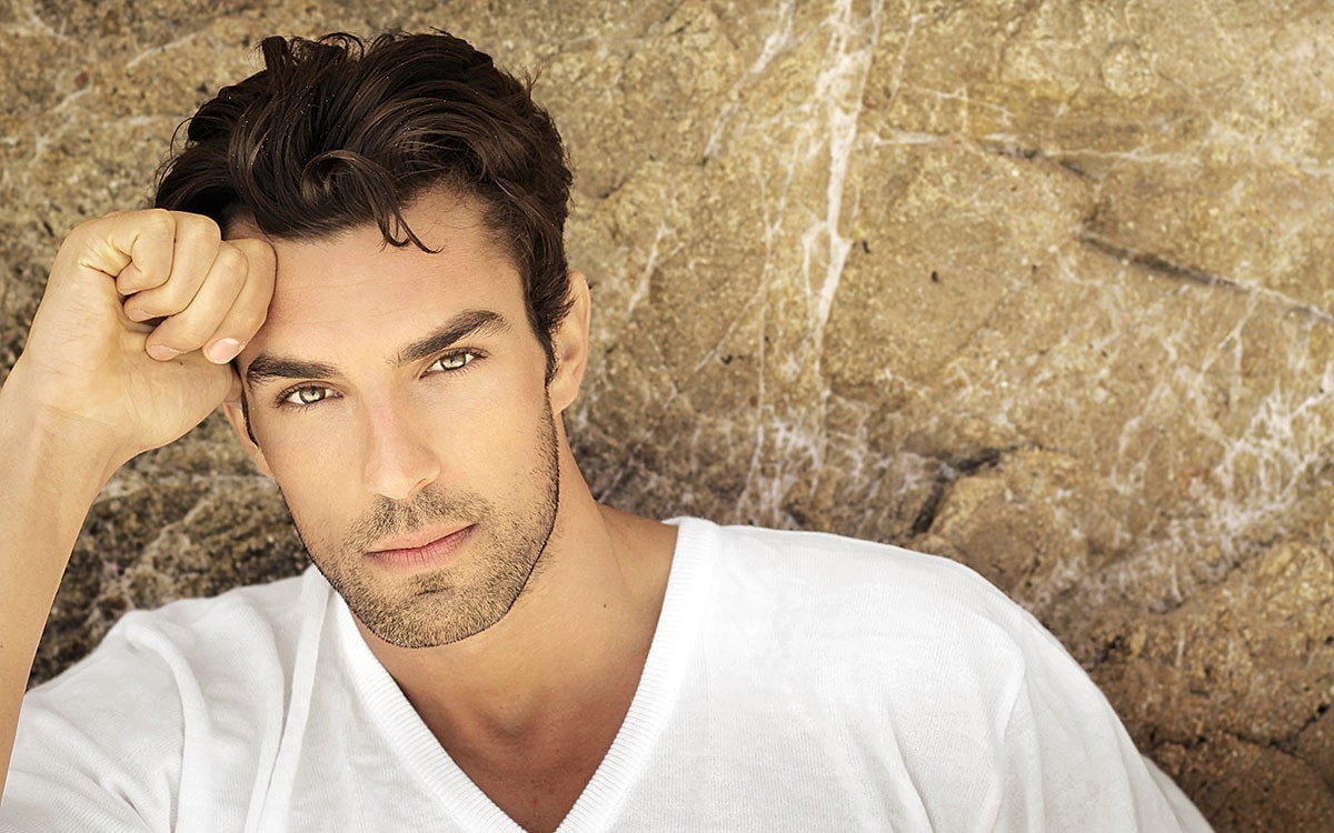 Man with tousled hair posing against rocks.