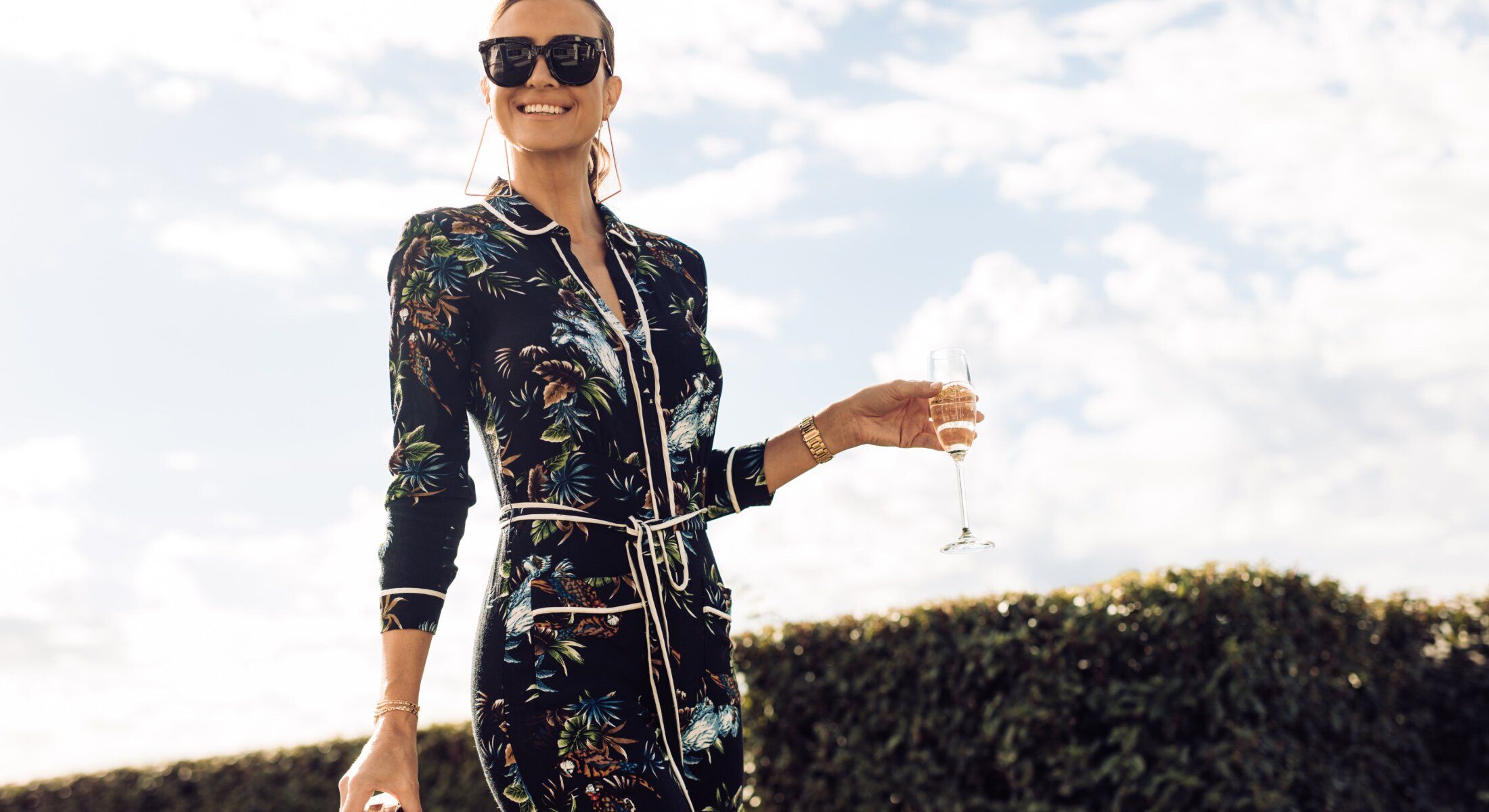 Woman in sunglasses holding champagne outdoors.