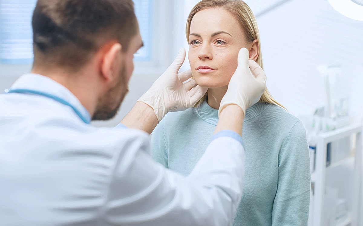 Doctor examining woman’s face in clinic.