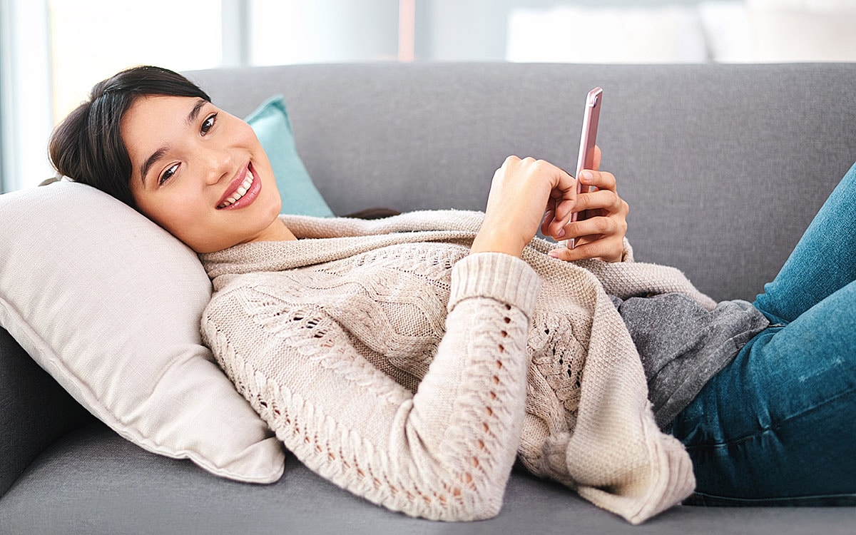 Smiling woman relaxing with smartphone on couch.