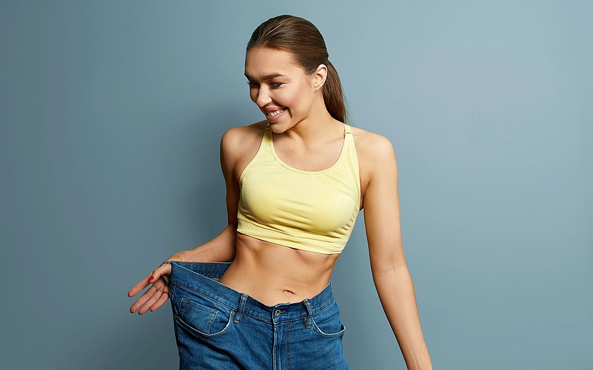 Woman smiling, holding oversized jeans, casual outfit.